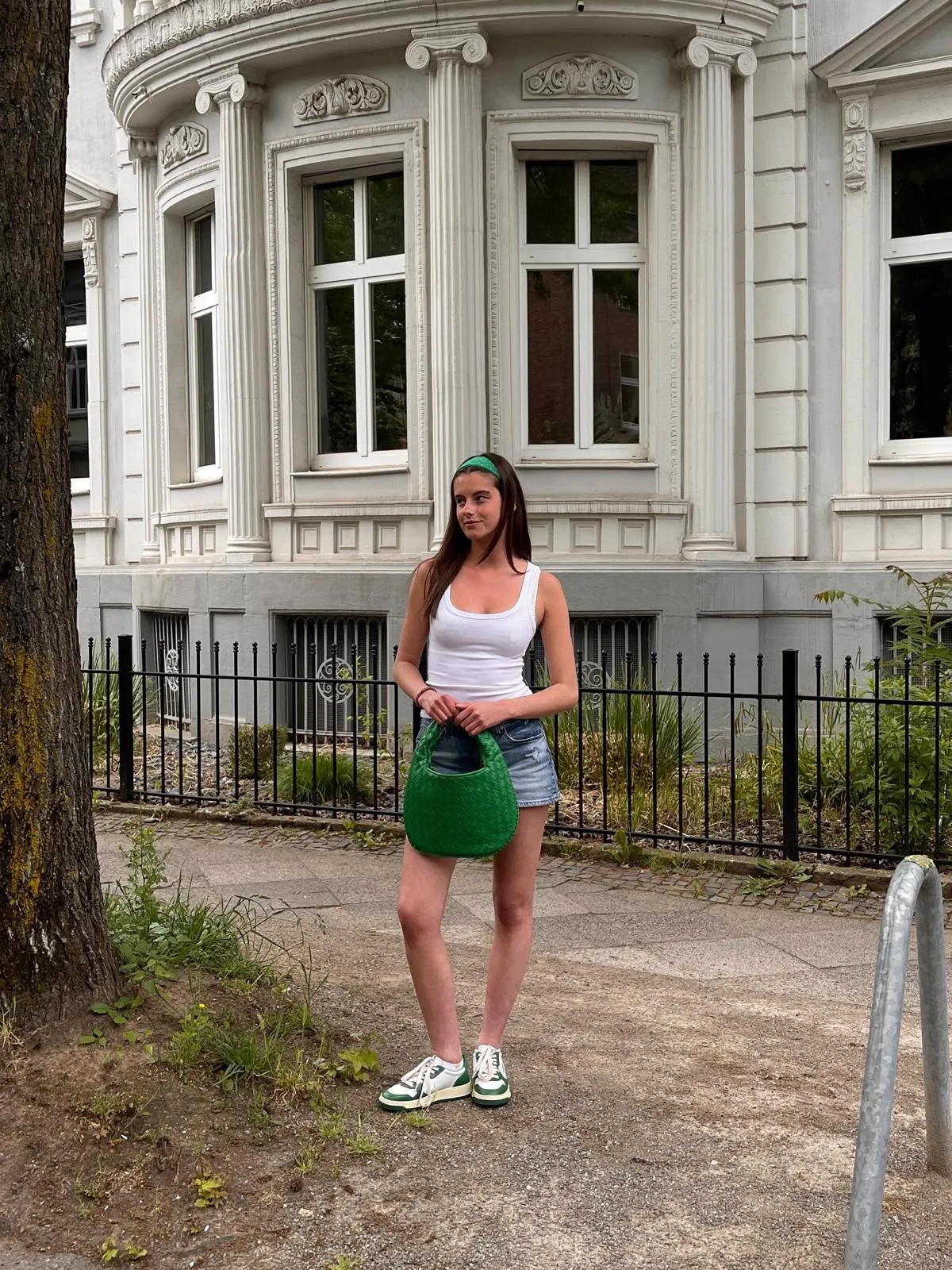 Jule in weißem Top mit grüner Flechttasche vor einer Altbaufassade